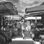 Group Discounts - Black and white of crowd of people strolling in market with different clothes and goods in daytime