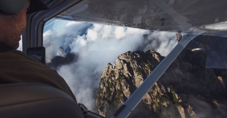 Flight Alerts - Man in Aircraft Looking at Rocky Mountain in Clouds