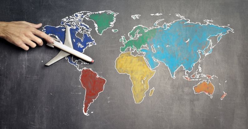 One-Way Flights - Top view of crop anonymous person holding toy airplane on colorful world map drawn on chalkboard