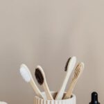 Budget-friendly Alternatives - Collection of bamboo toothbrushes and organic natural soaps with wooden body brush arranged with recyclable glass bottle with natural oil and ceramic vase with artificial plant