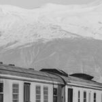 Overnight Train - A black and white photo of a train with snow capped mountains in the background