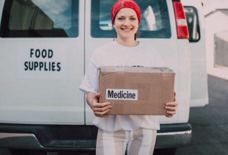 Volunteer Travel - Woman Carrying a Medicine Labelled Cardboard Boxes Behind a White Van