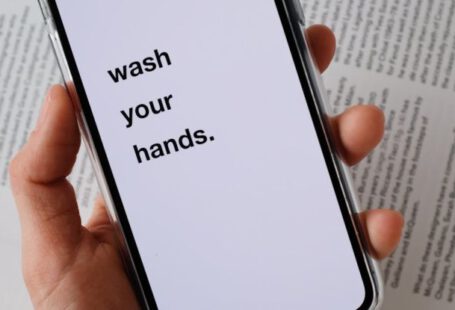 Secure Your Belongings - From above of unrecognizable person taking modern cellphone with WASH YOUR HANDS inscription on blank screen placed under page of book illustrating hygiene concept